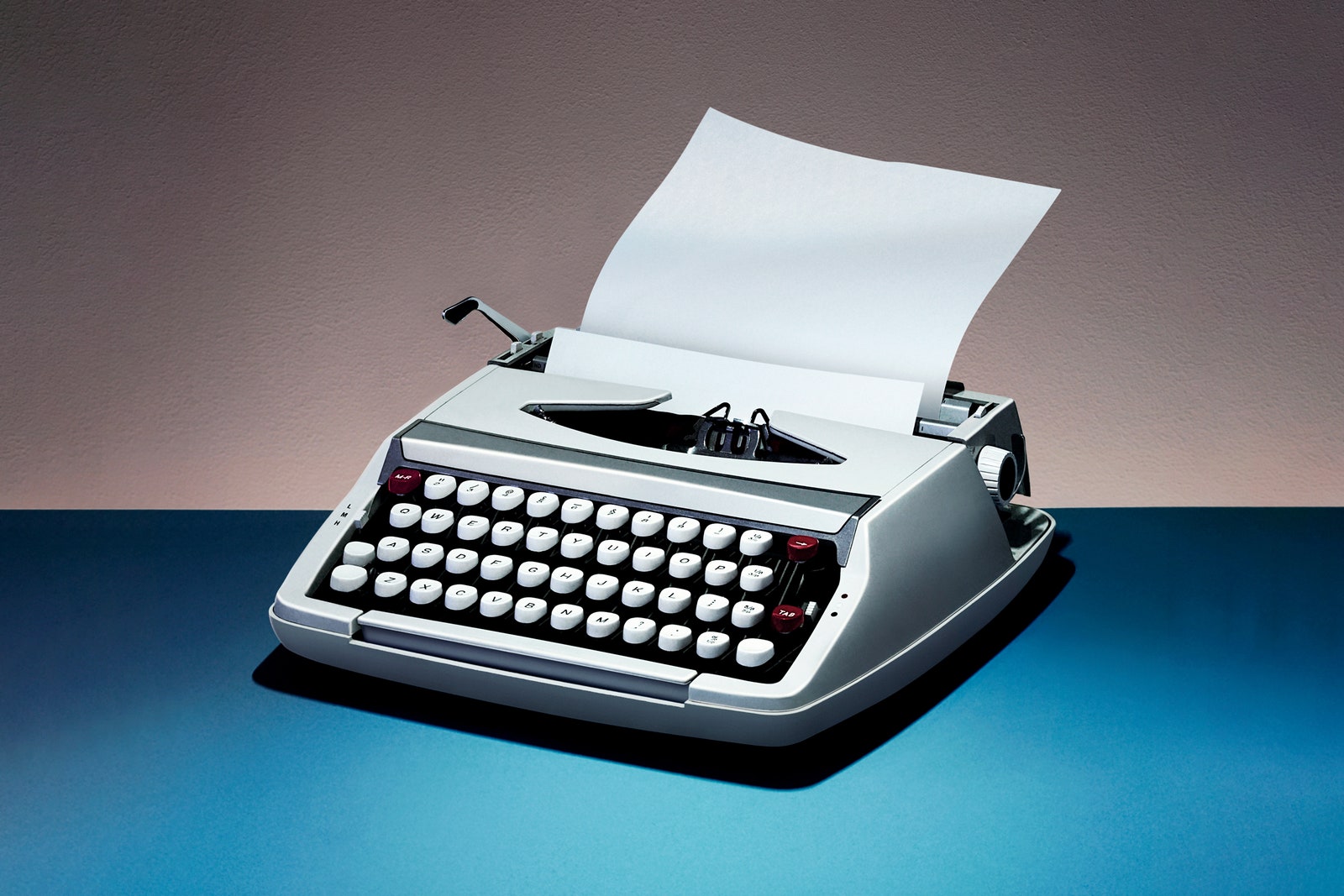 A typewriter on a blue table with one blank piece of paper coming out