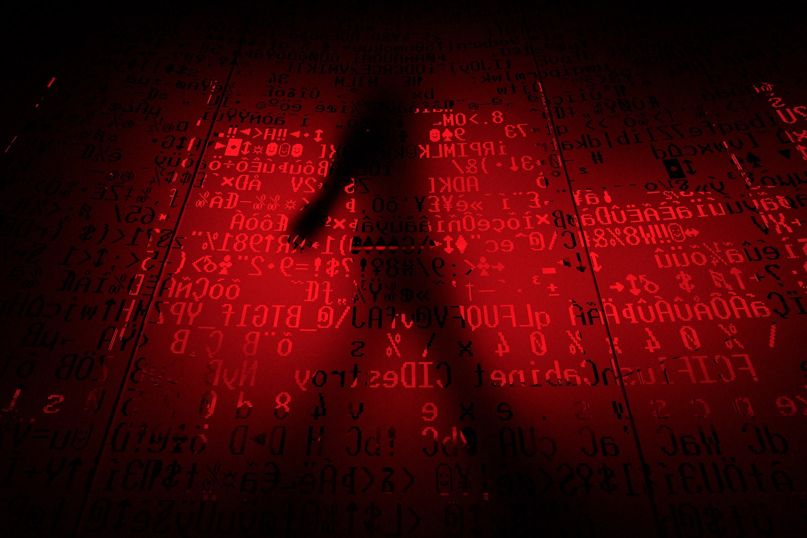 Silhouetted person walks behind a glass window that has computer code inscribed on it