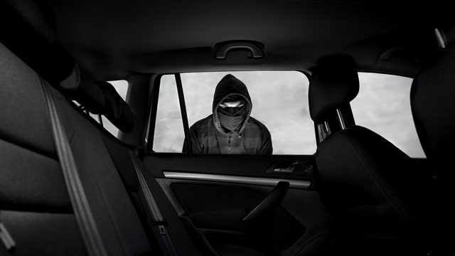 Thief with a face covering staring into a car window