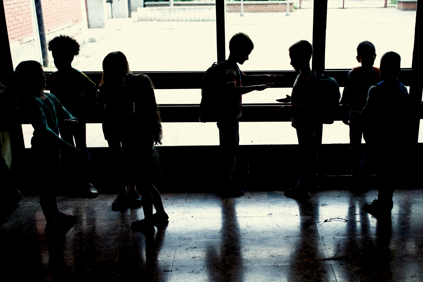Silhouettes of a group of school children standing in a hallway playing together and communicating